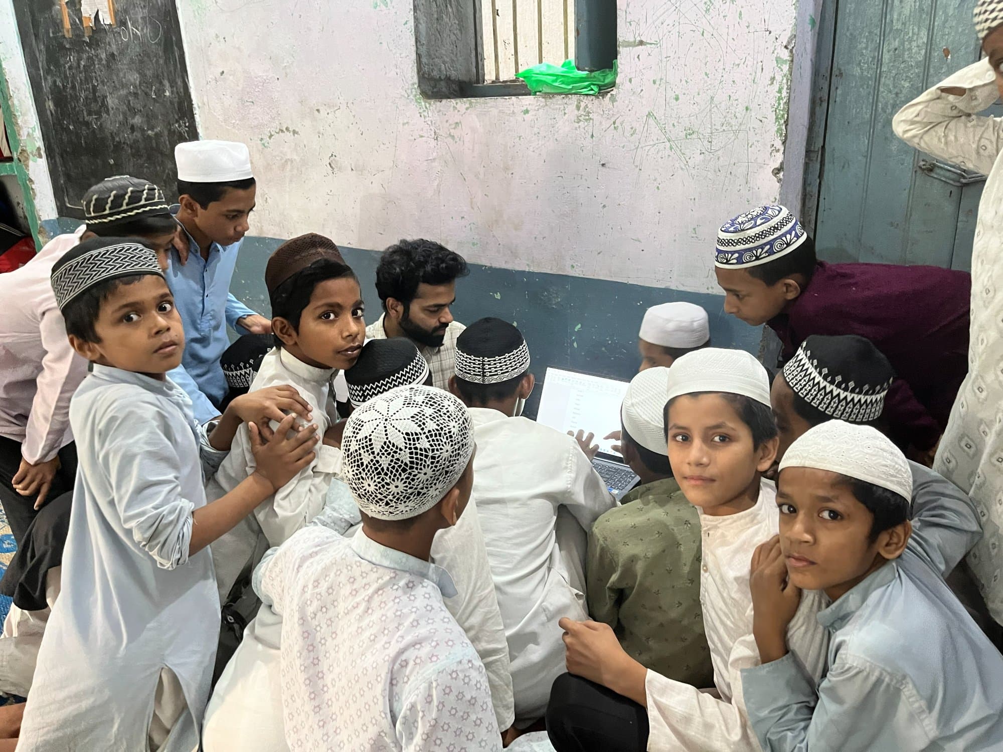 Madarsa students during a digital-literacy session, some following the laptop screen and some looking at the camera.
